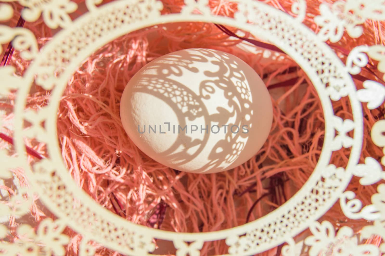 Easter card with egg and white openwork oval frame on coral background, Bright sunlight creates beautiful shadows on white egg, copyspace, top view