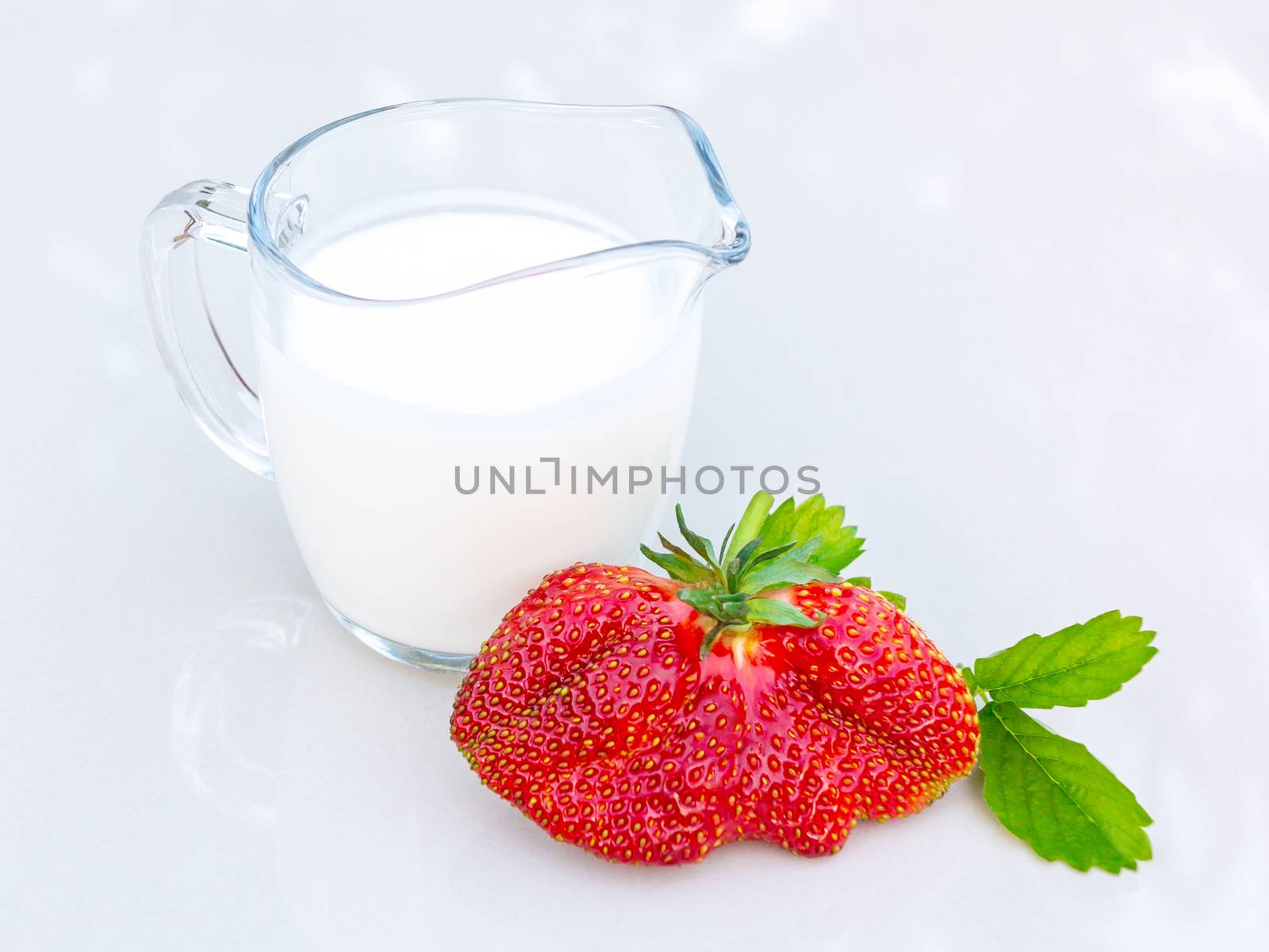 A huge ripe strawberry and cream sauce on the table on a bright table by galsand