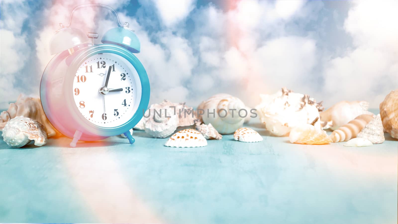 Seashell border and an alarm clock on a blue table against a blue sky with clouds - summer holidays and vacation time concept, copy space, place for text by galsand