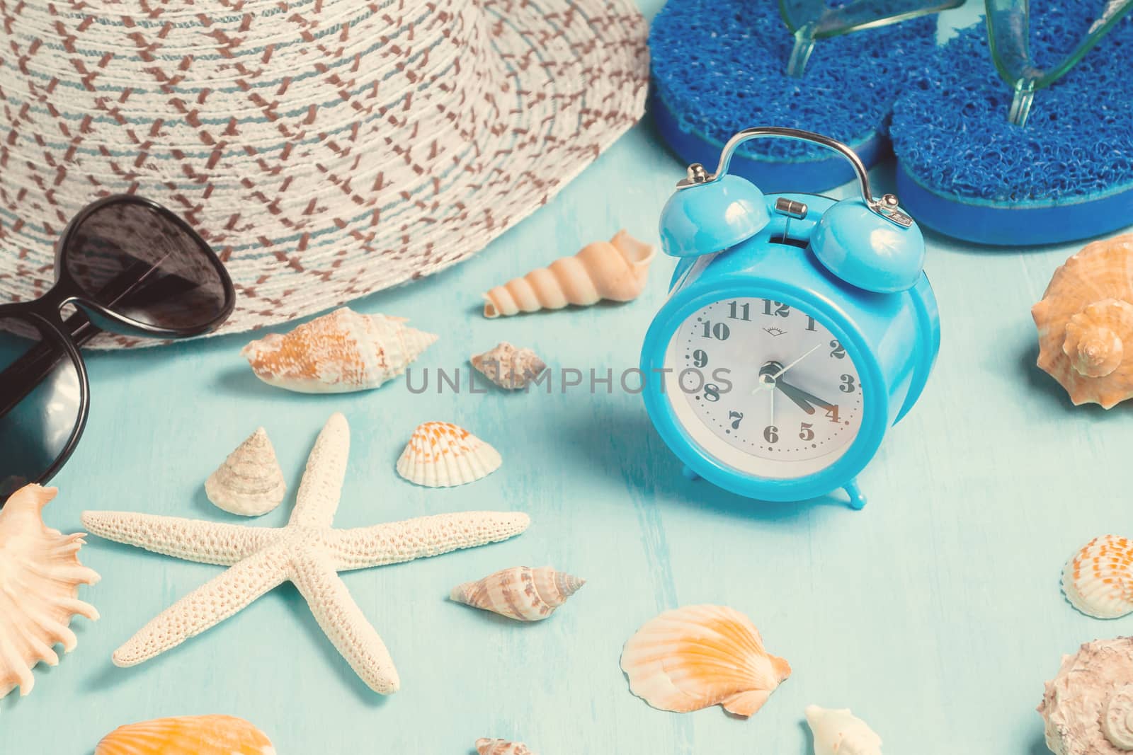 Seashells, alarm clock and beach accessories on a blue table - summer vacation and vacation time concept by galsand