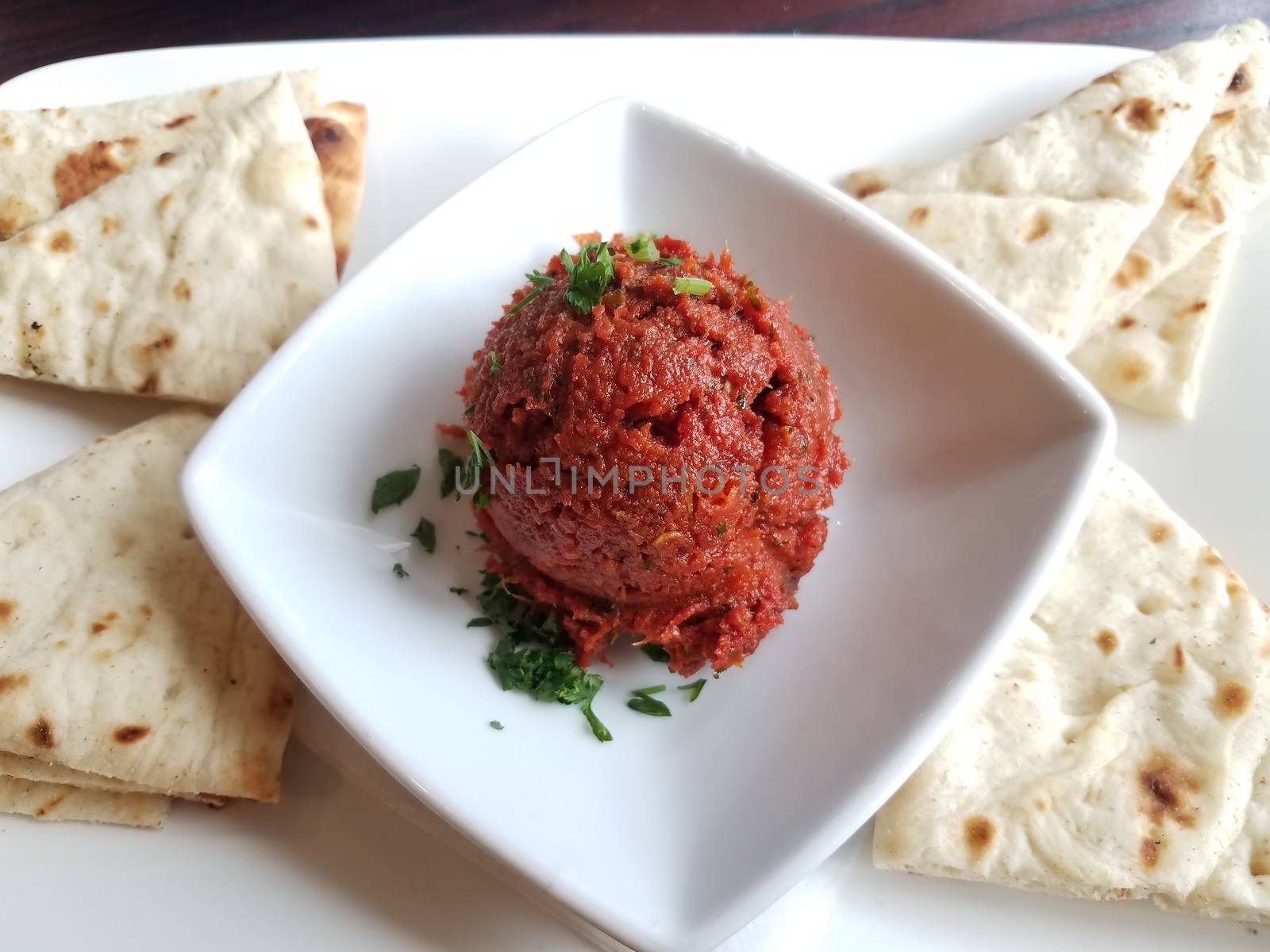 spicy red Greek mediterranean dip with bread triangles on white plate