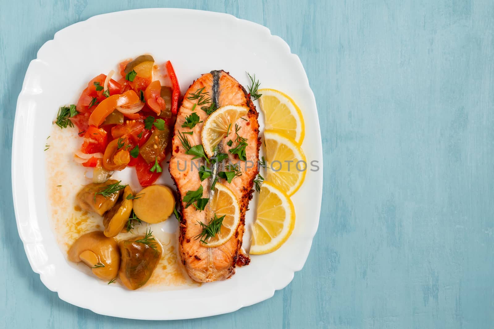Baked salmon fillet medallion with salad of pickled vegetables and mushrooms on a white plate on a blue background, top view, flatlay, place for text, copy space by galsand