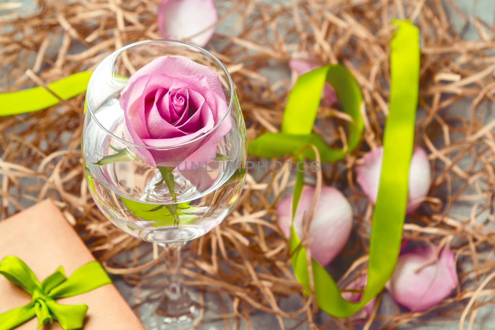 Pink rose in a glass with water and decorations on the table.