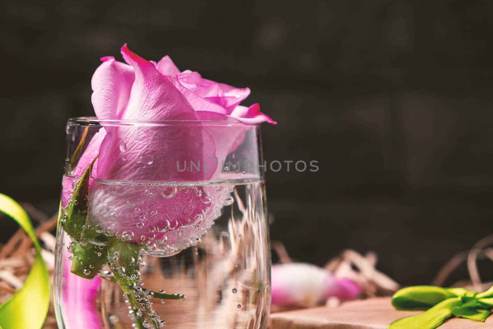 Pink rose in a glass with water and decorations on the table by galsand