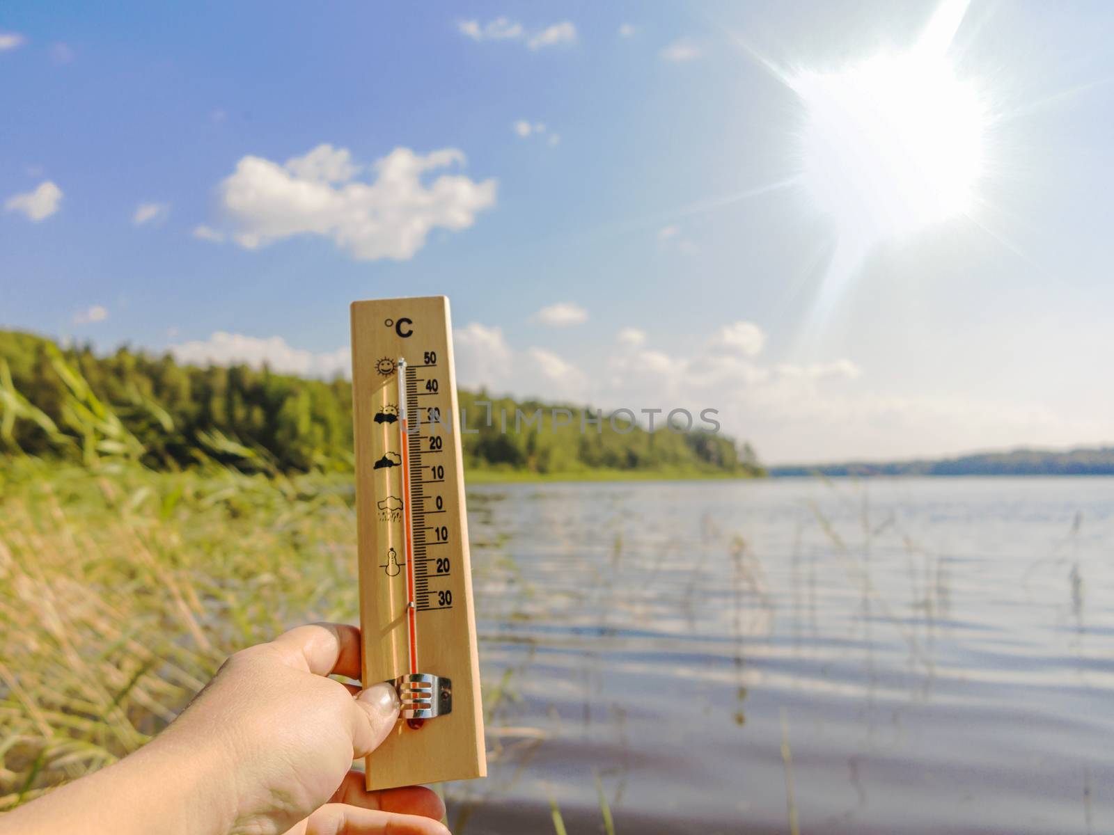 Thermometer showing 30 degrees Celsius of heat against the background of the lake water and the blue sky in sunlight by galsand