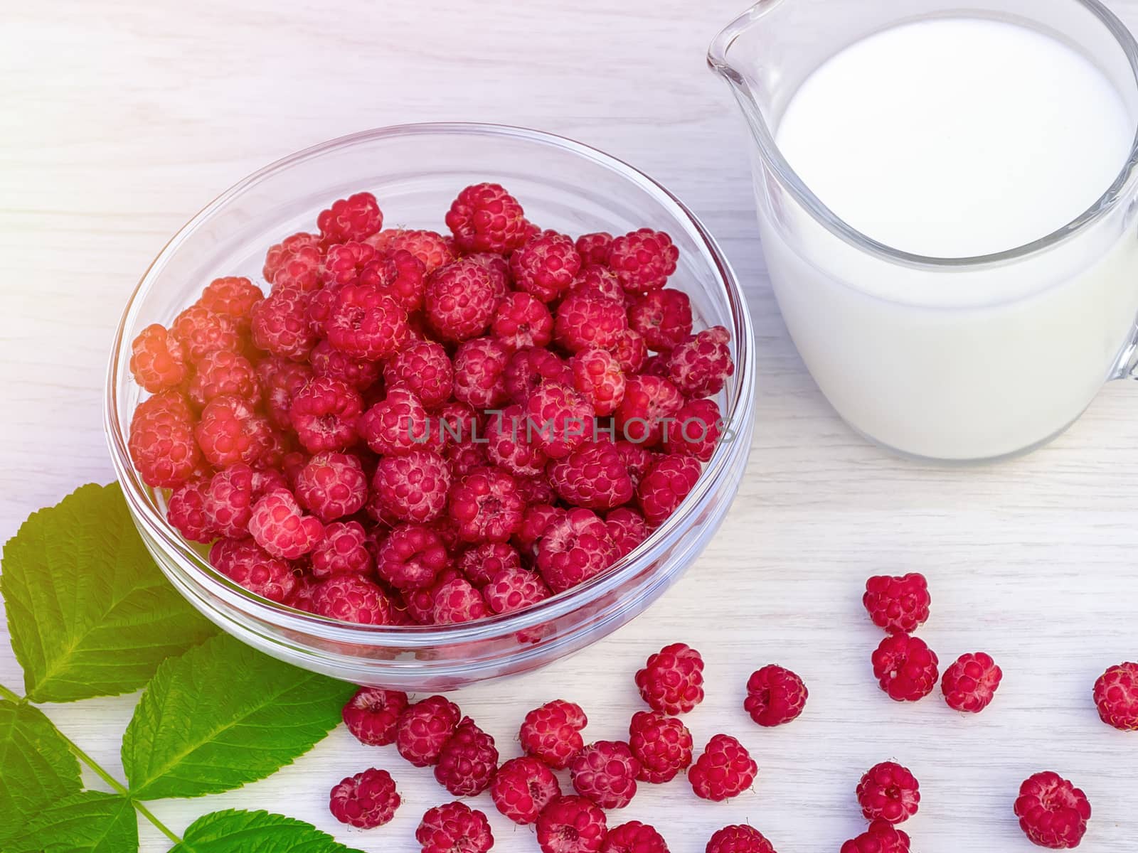 Fresh raspberries in a glass bowl and natural iogurt on a white wooden table. Healthy eating concept by galsand