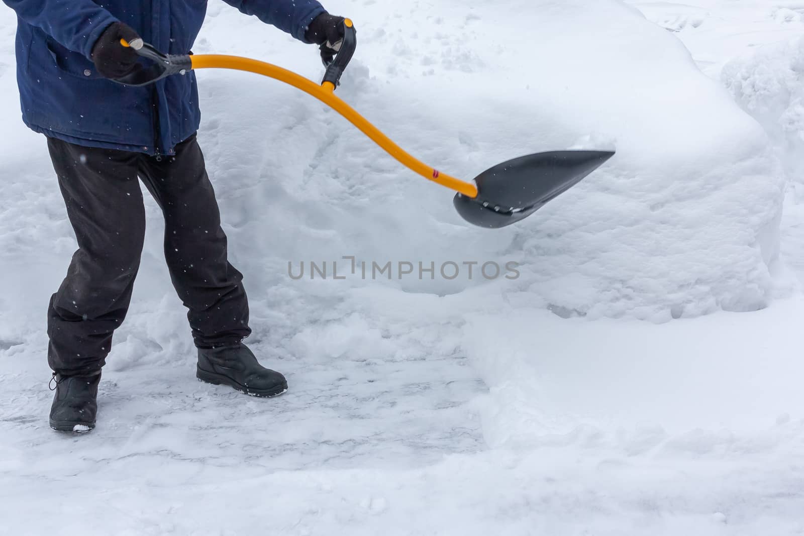 A man cleans snow in the yard with a shovel after a heavy snowfall by galsand