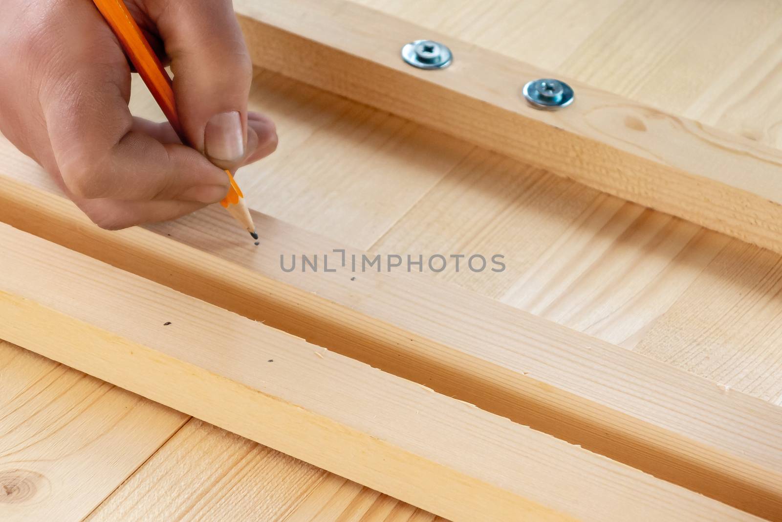 Male hands are marking boards for drilling holes for screws.