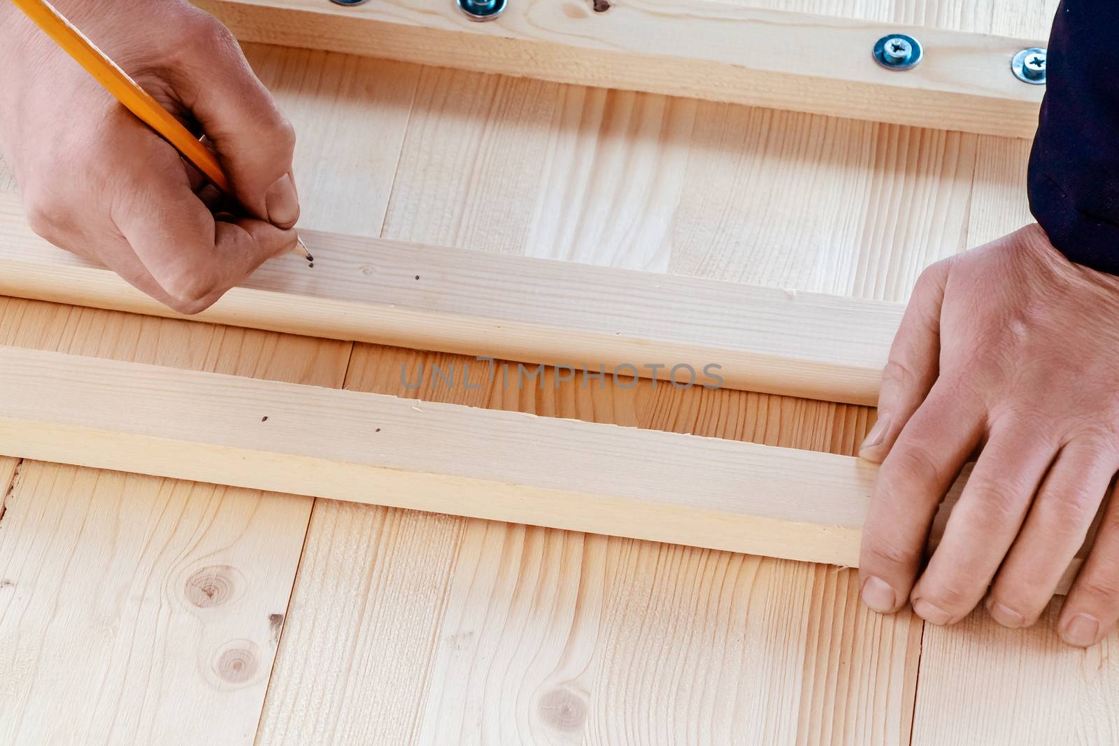 Male hands are marking boards for drilling holes for screws.