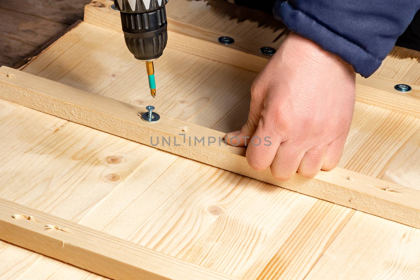 Male hands screw wooden blocks to the boards with a screwdriver.