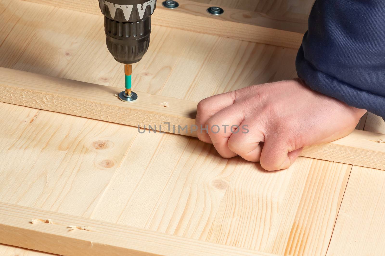 Male hands screw wooden blocks to the boards with a screwdriver by galsand