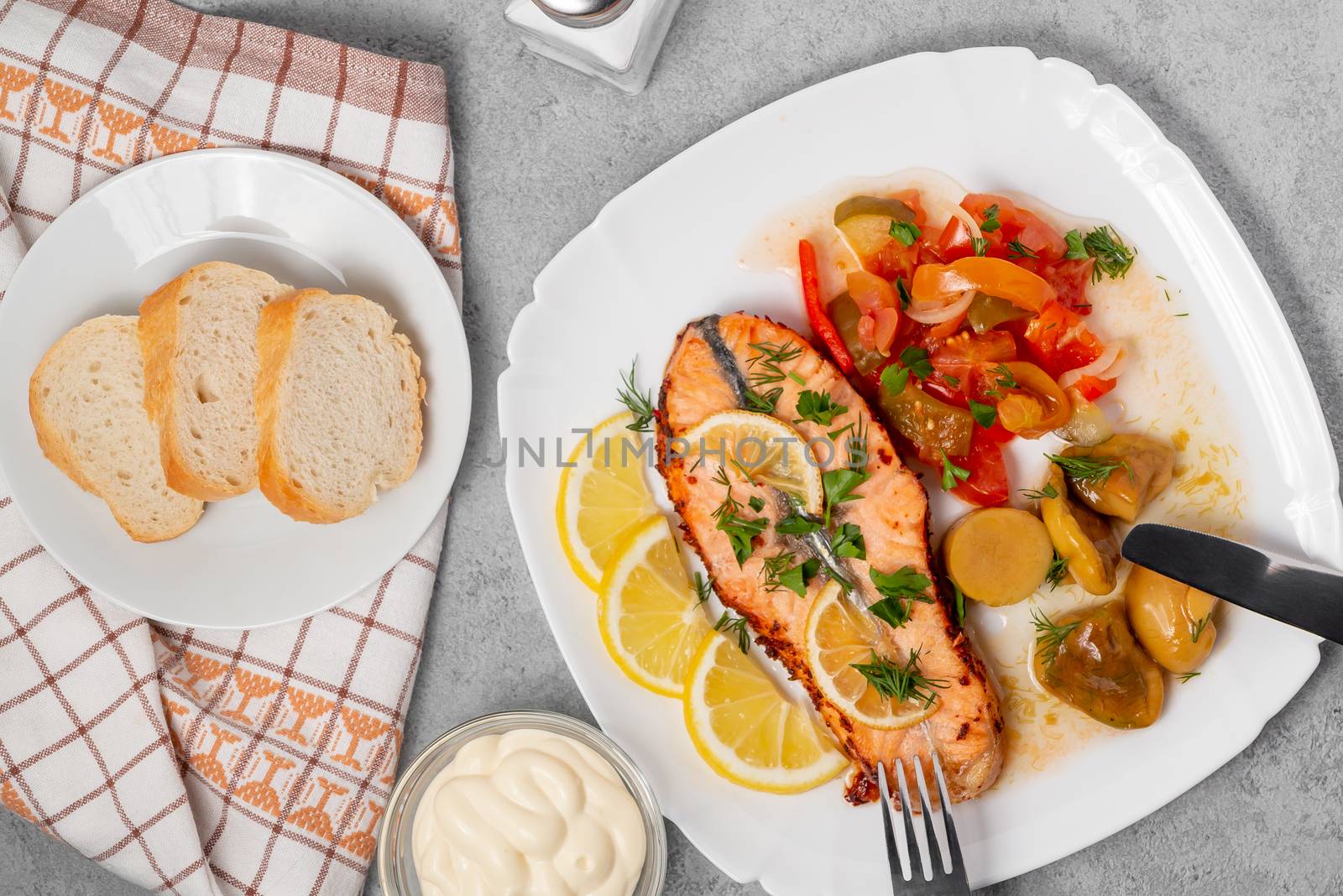 Baked salmon fillet medallion with salad of pickled vegetables and mushrooms on a white plate on a gray background, top view, flatlay by galsand