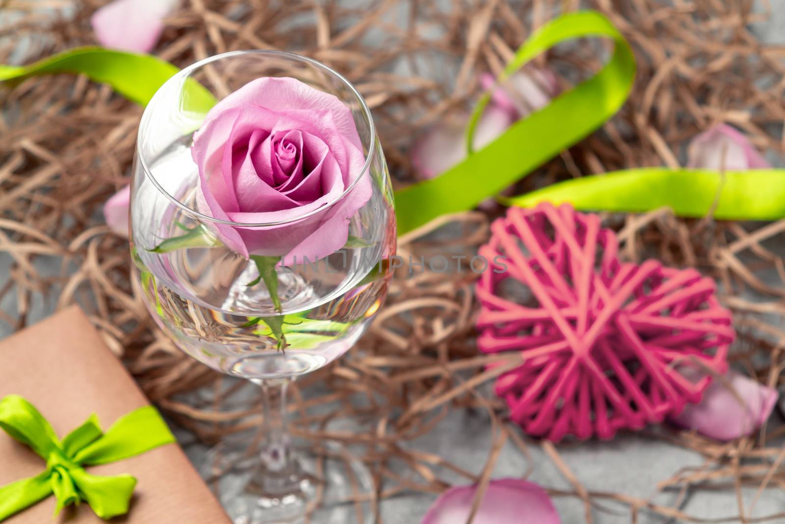 Pink rose in a glass with water and decorations on the table by galsand