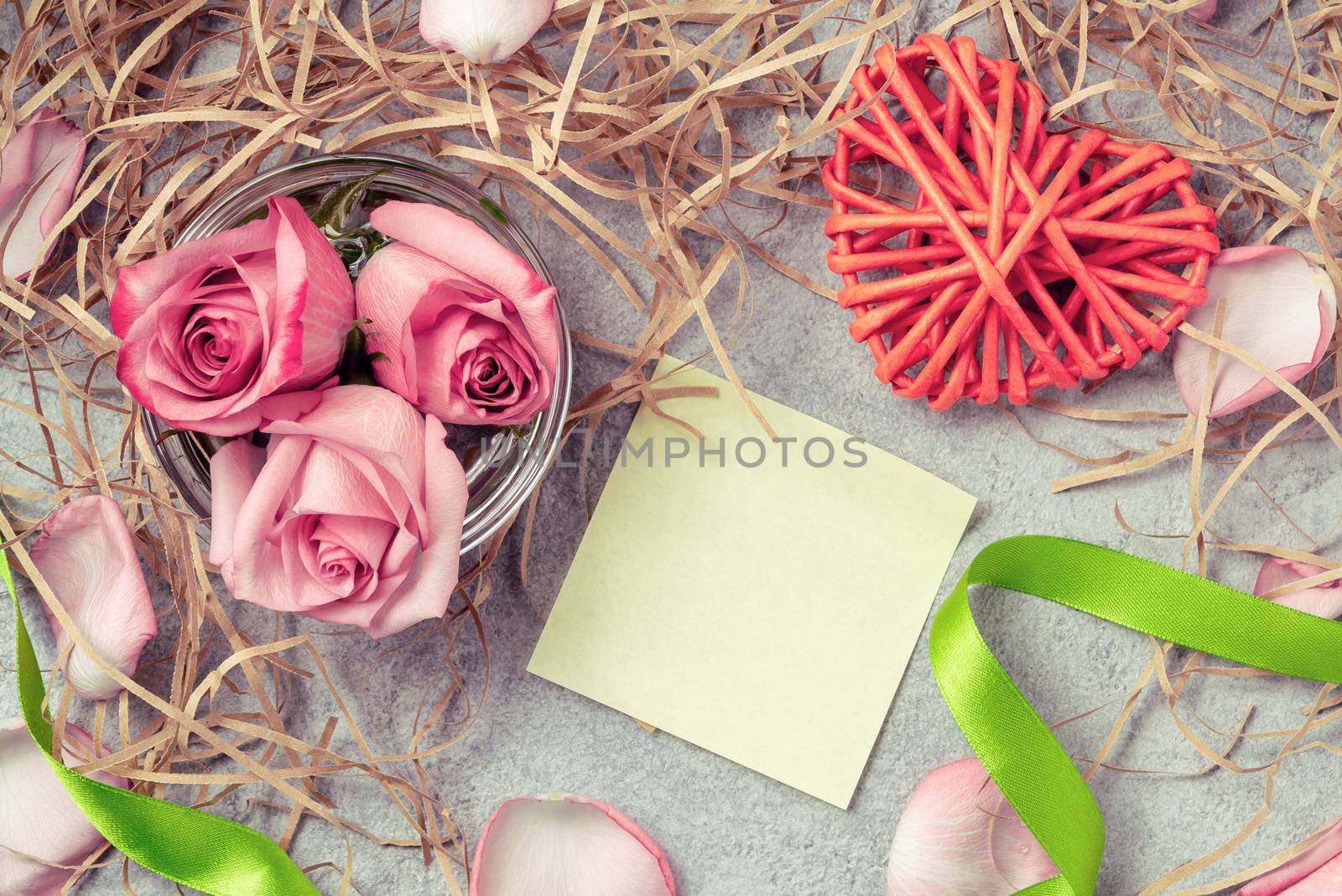 Pink roses in the water, a wicker heart, ornaments and an empty form for a note on the table.