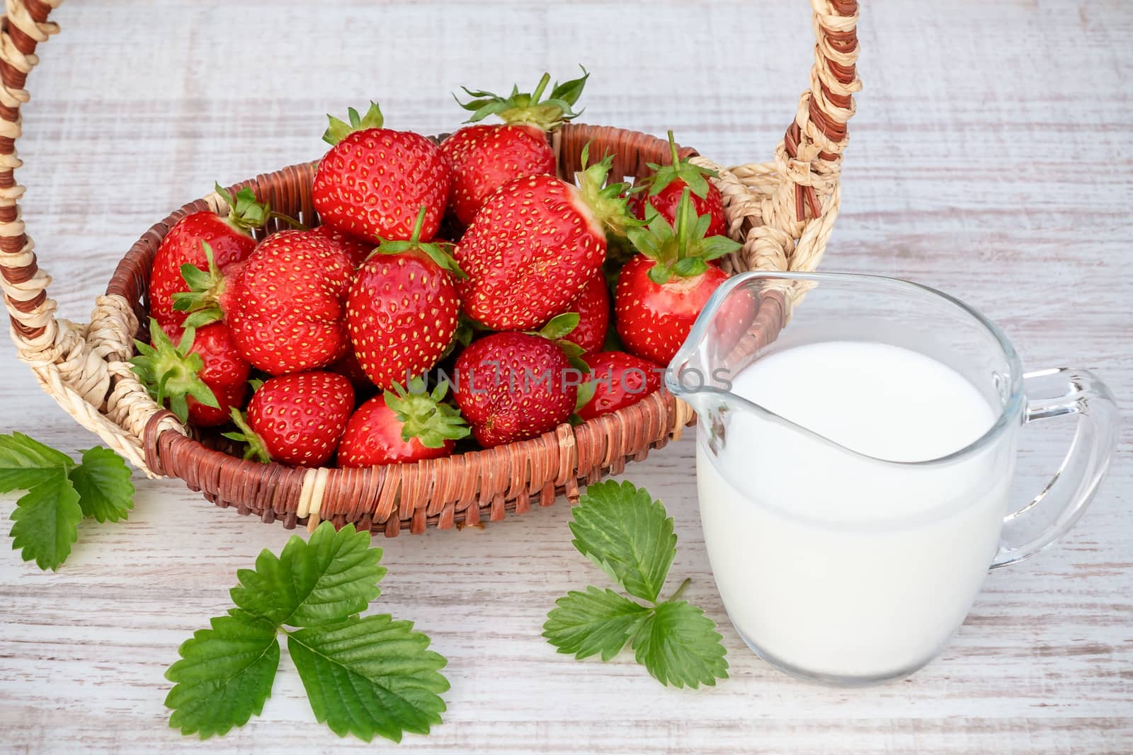 Fresh ripe strawberries in a basket and iogurt on a wooden table outdoors on a summer day by galsand