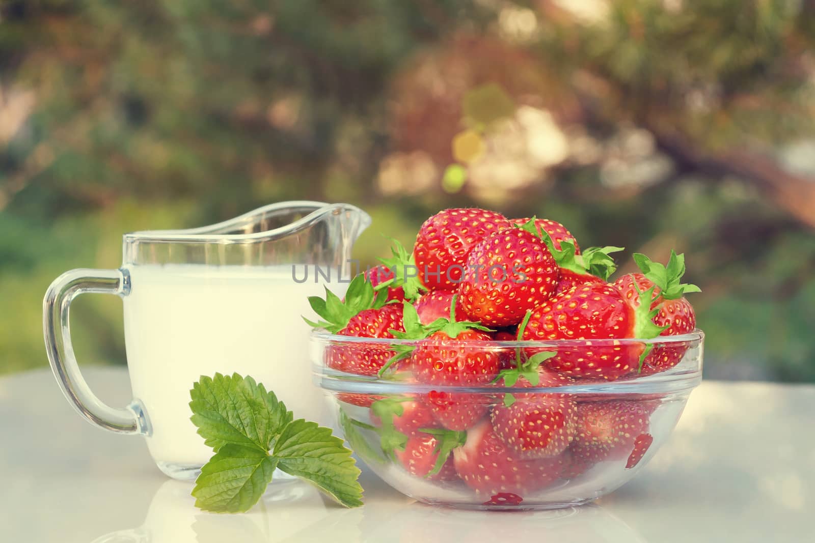 Fresh ripe strawberries in a bowl and iogurt on a white table outdoors on a summer day.
