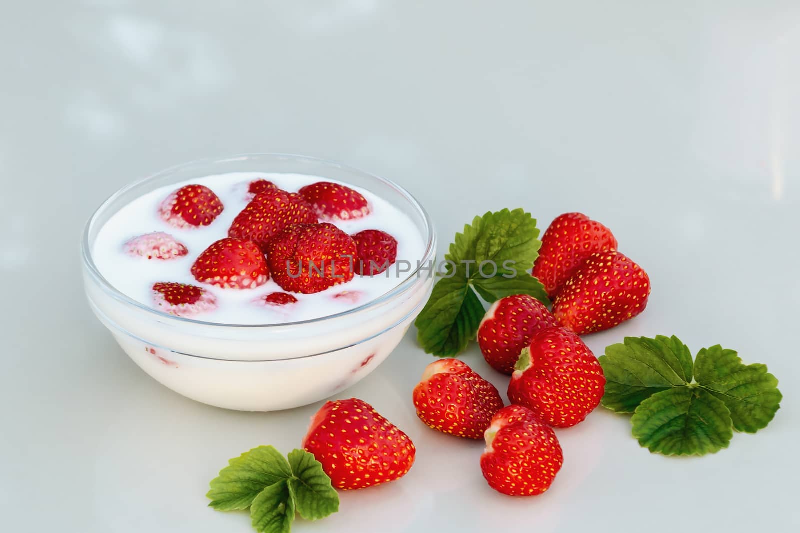 Fresh ripe strawberries in a bowl with yogurt on a white table outdoors on a summer day by galsand