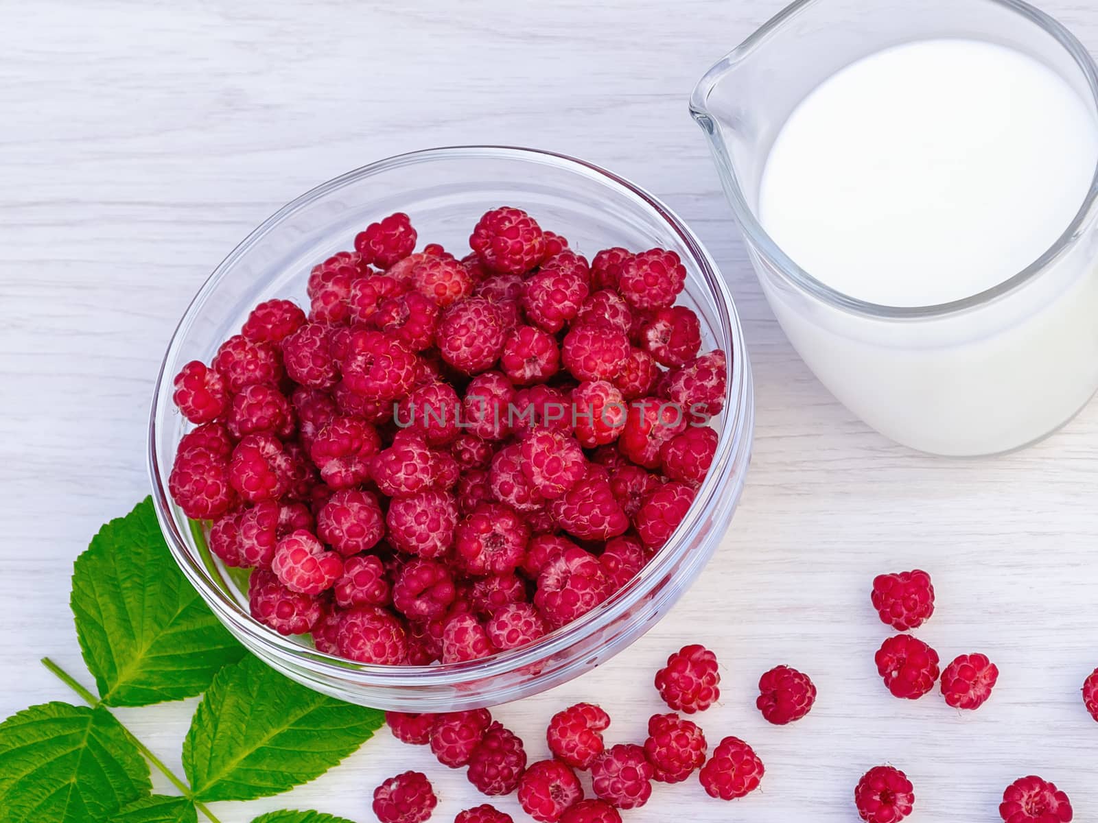 Fresh raspberries in a glass bowl and natural iogurt on a white wooden table. Healthy eating concept.