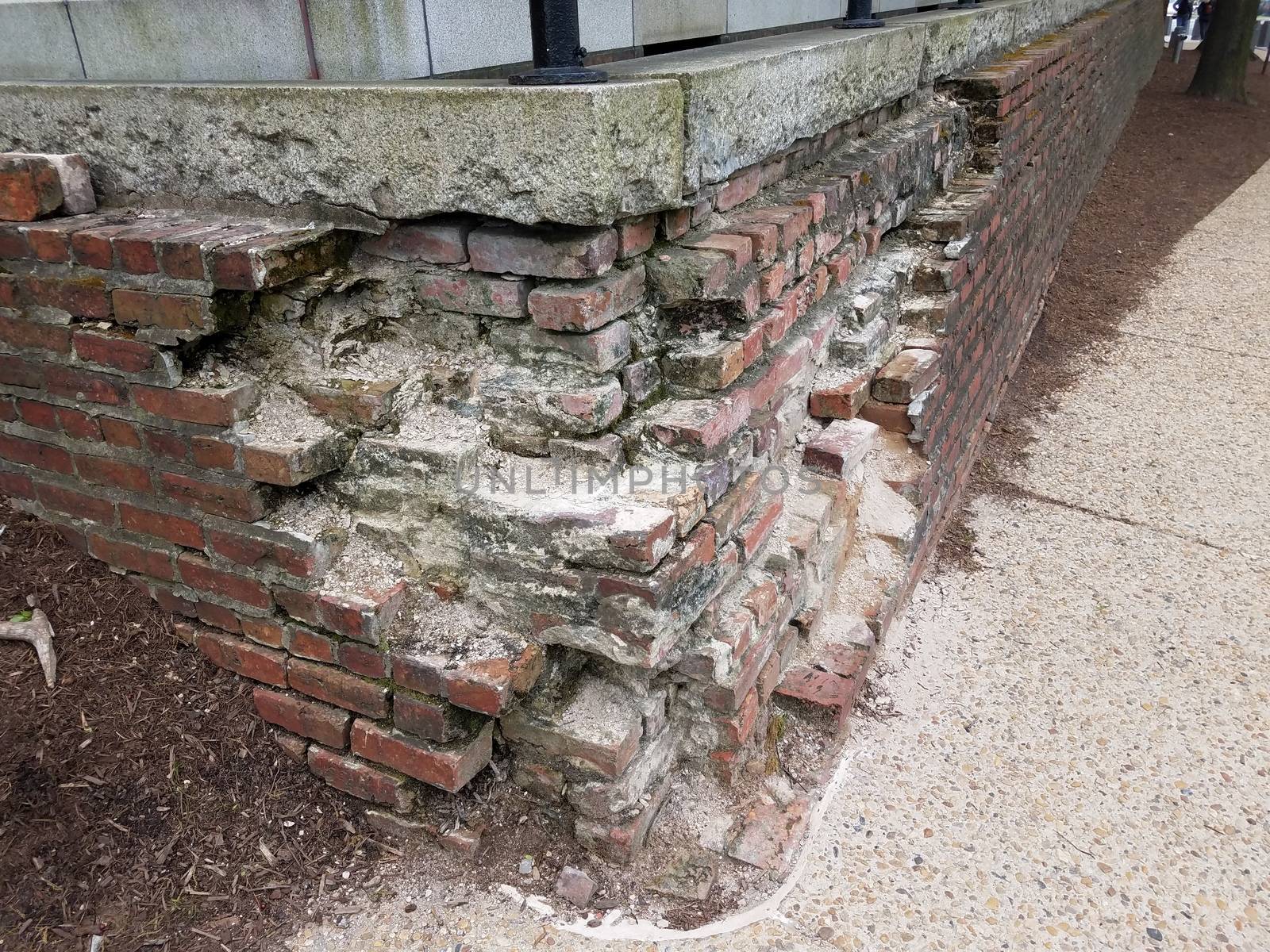 broken or damaged brick wall or masonry with cement sidewalk