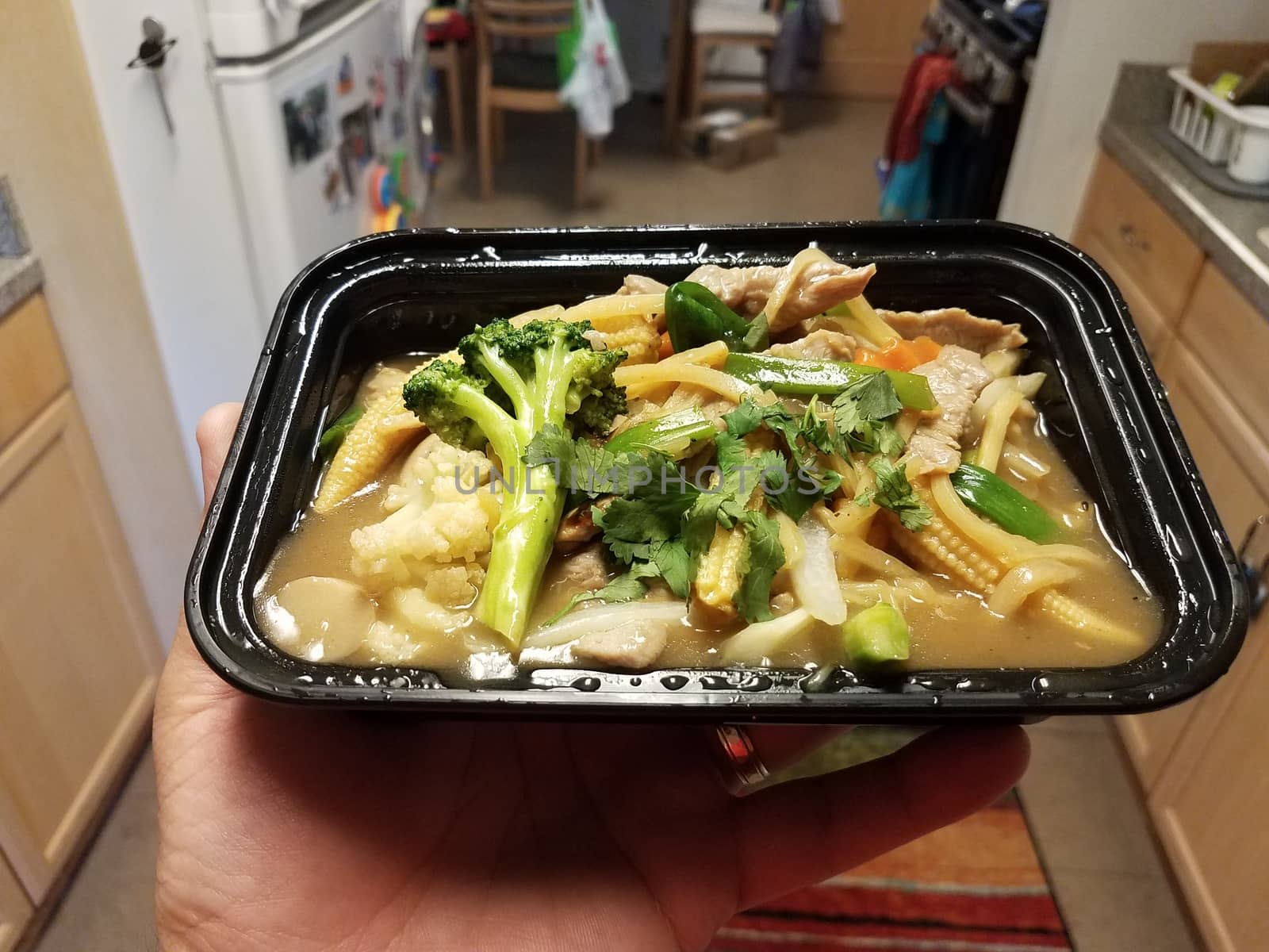 hand holding Thai food with curry broccoli bamboo and pork and corn