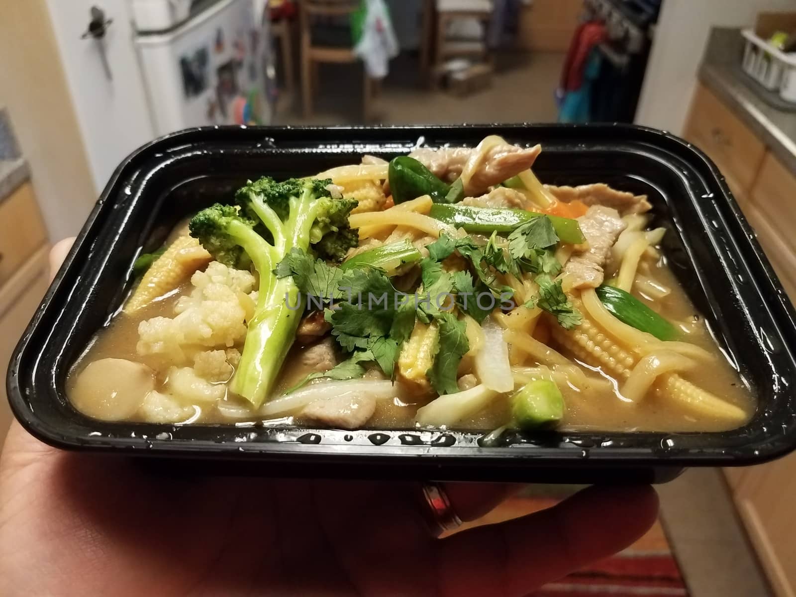 hand holding Thai food with curry broccoli bamboo and pork and corn