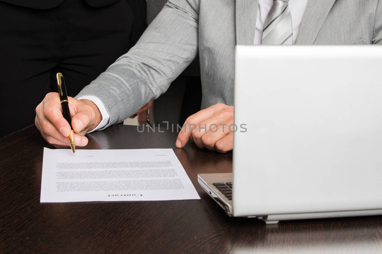 Close up photo of businessman sitting at office desk in front of laptop and singing contract document