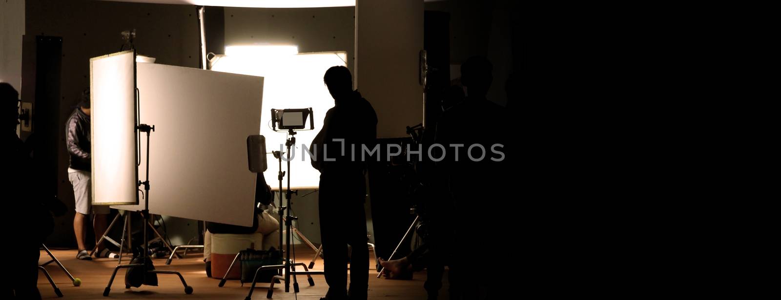 Shooting studio behind the scenes in silhouette images which film crew team working for filming movie or video with professional lighting and equipment such as camera, tripod, soft box, monitor