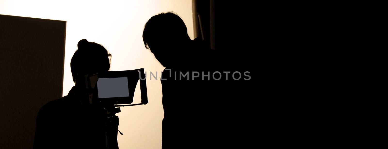 Shooting studio behind the scenes in silhouette images which film crew team working for filming movie or video with professional lighting and equipment such as camera, tripod, soft box, monitor