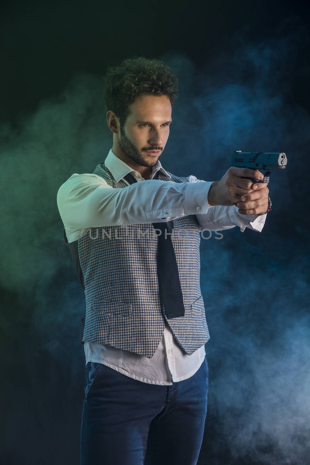 Elegant man with gun, pointing it at someone off frame, on smoky dark background
