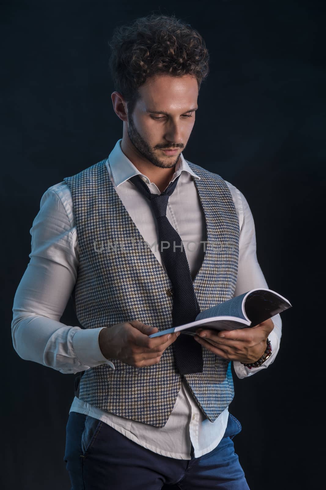 Elegant man reading a book in studio shot, standing on black background