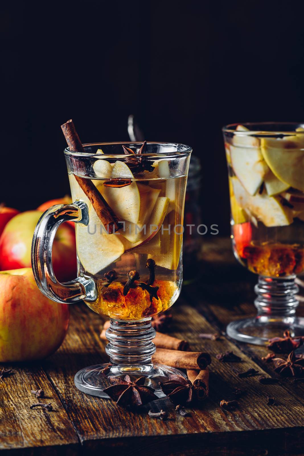 Two Glasses of Christmas Mulled Wine with Sliced Apple, Clove, Cinnamon, Anise Star and Dark Candy Sugar. All Ingredients and Some Kitchen utensils on Wooden Table.Vertical.