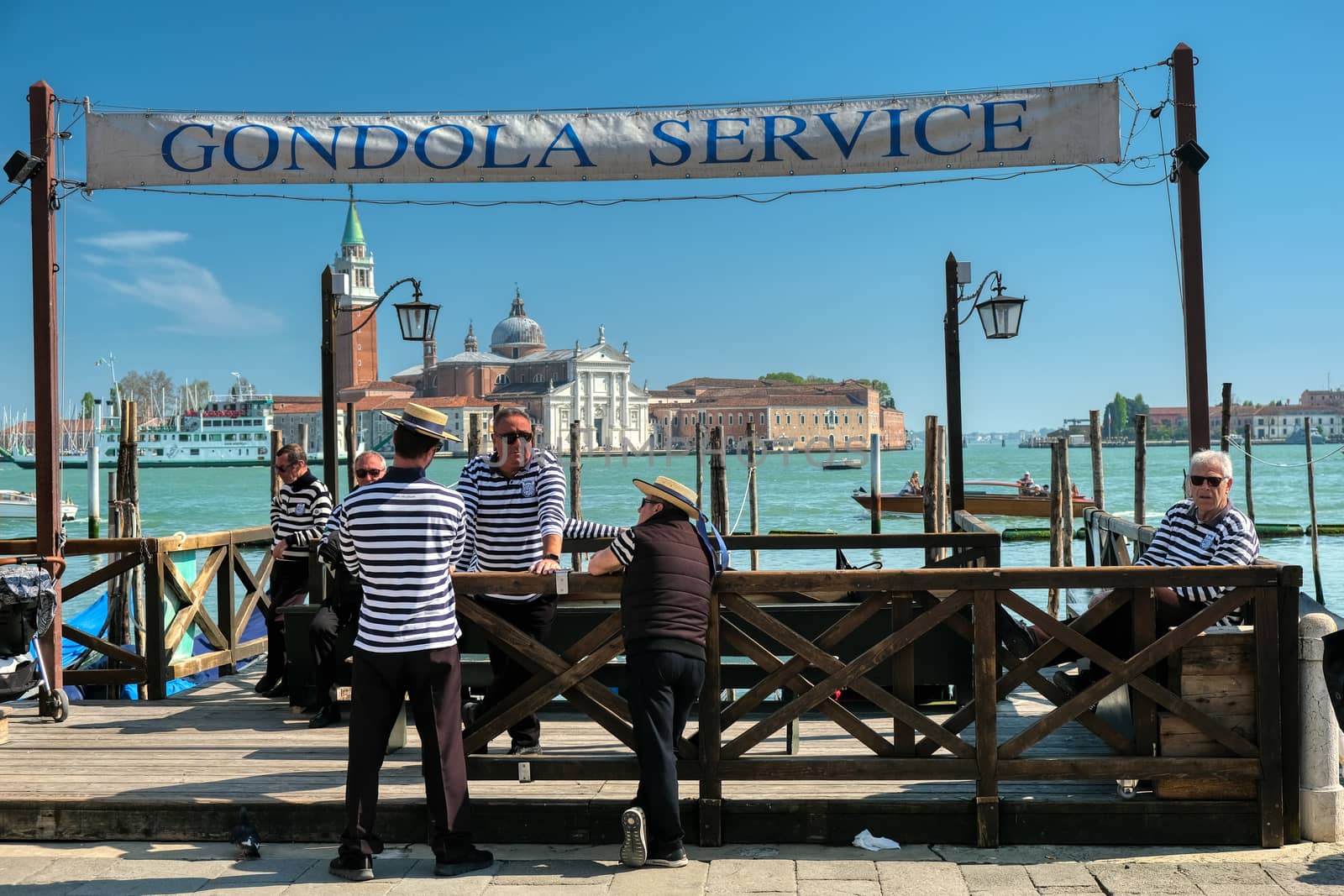 Venice, Italy - April 17 2019: Gondoliers waiting at gondola service for customers at Saint Mark's square in Venice with San Georgio Maggiore church in background