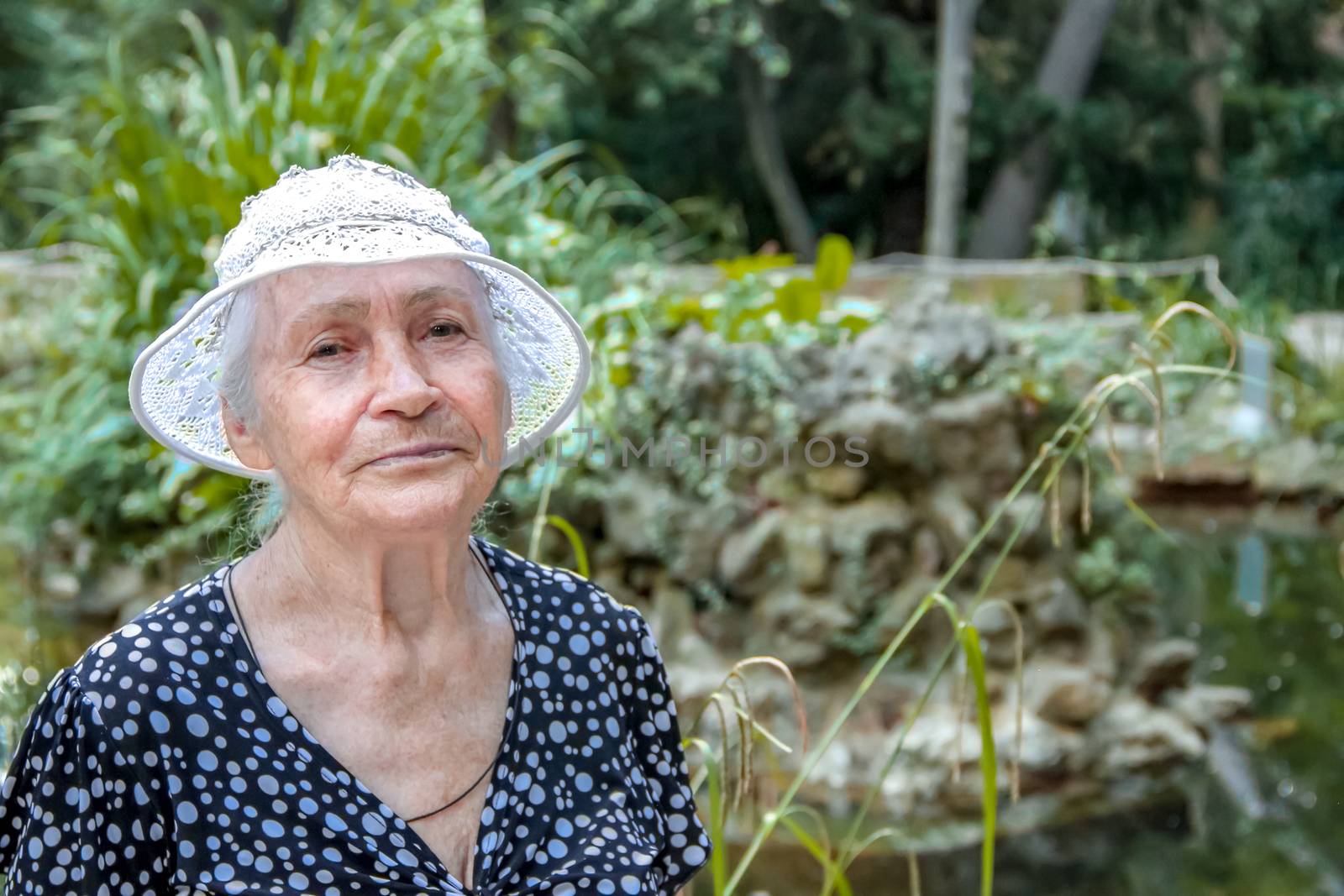 Closeup portrait of a serene senior woman in a knitted white hat, standing outside in summer