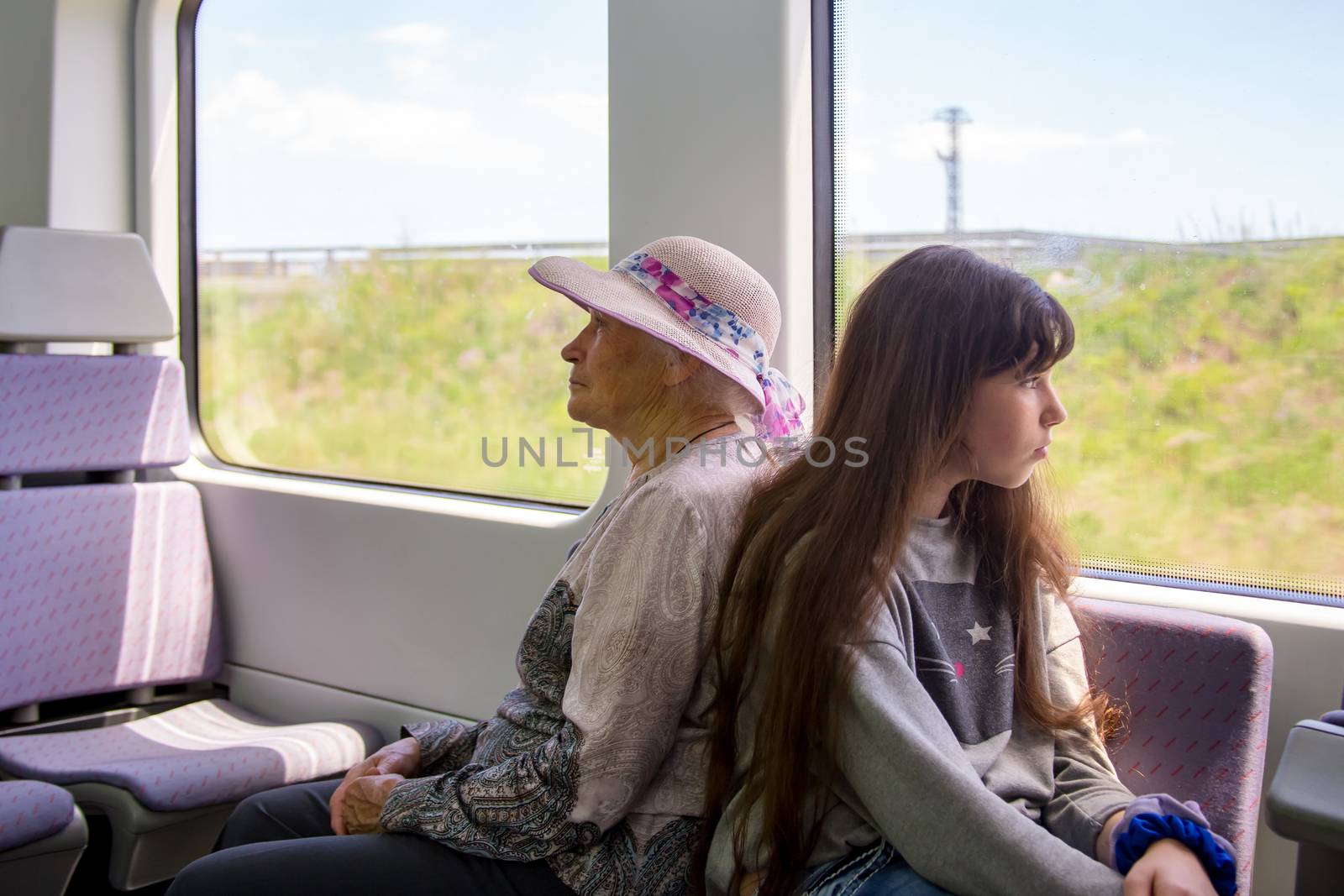 Beautiful gray-haired grandmother in a sun hat rides an electric train with her teenage granddaughter and looks out the window.