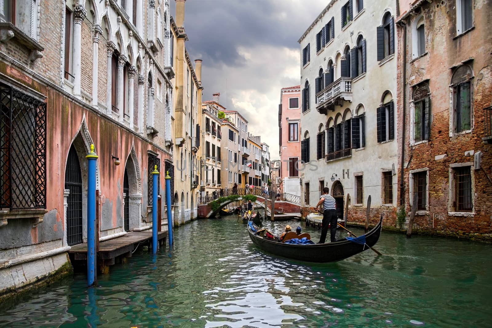 Gondolier on ornamental boat in channel water in Venice