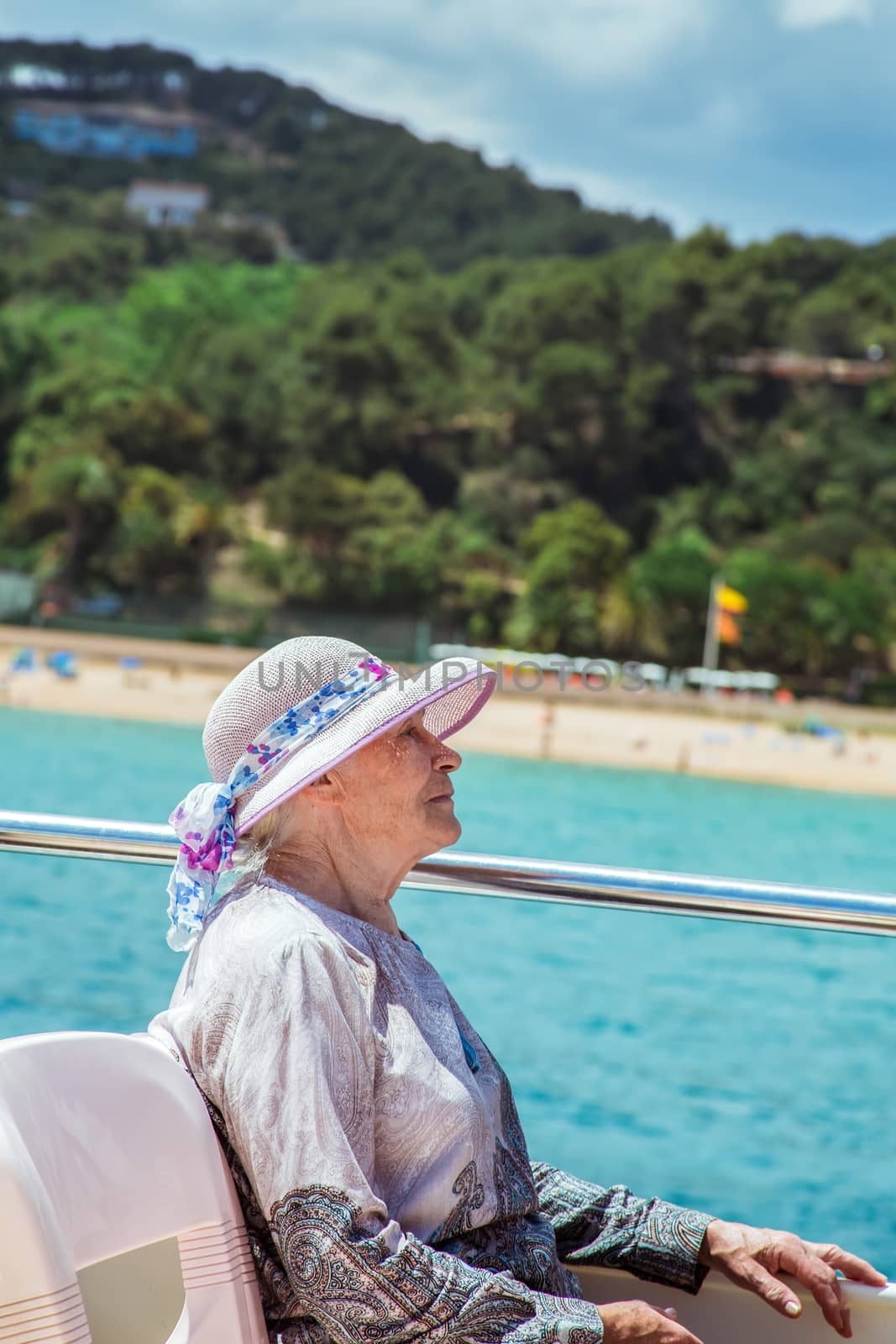 Elderly pretty woman in sun-hat enjoys summer vacation in a sea voyage on a pleasure boat. She sits on the upper deck