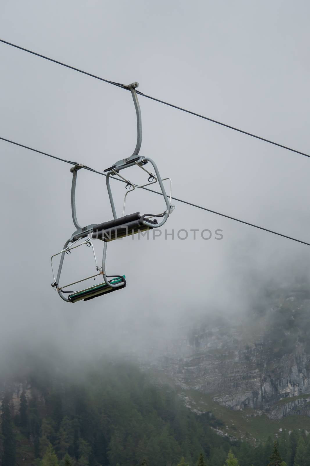 A chairlift with mountains and fog in the background by sandra_fotodesign