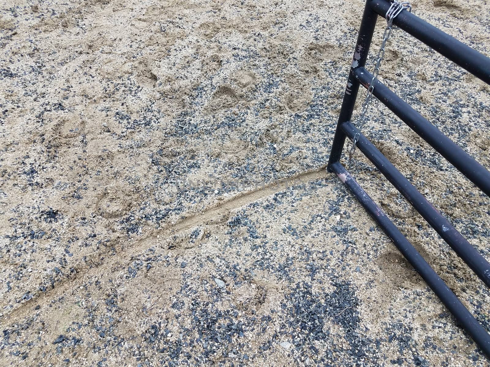 black metal fence or gate with trail in ground or sand and horse shoe prints