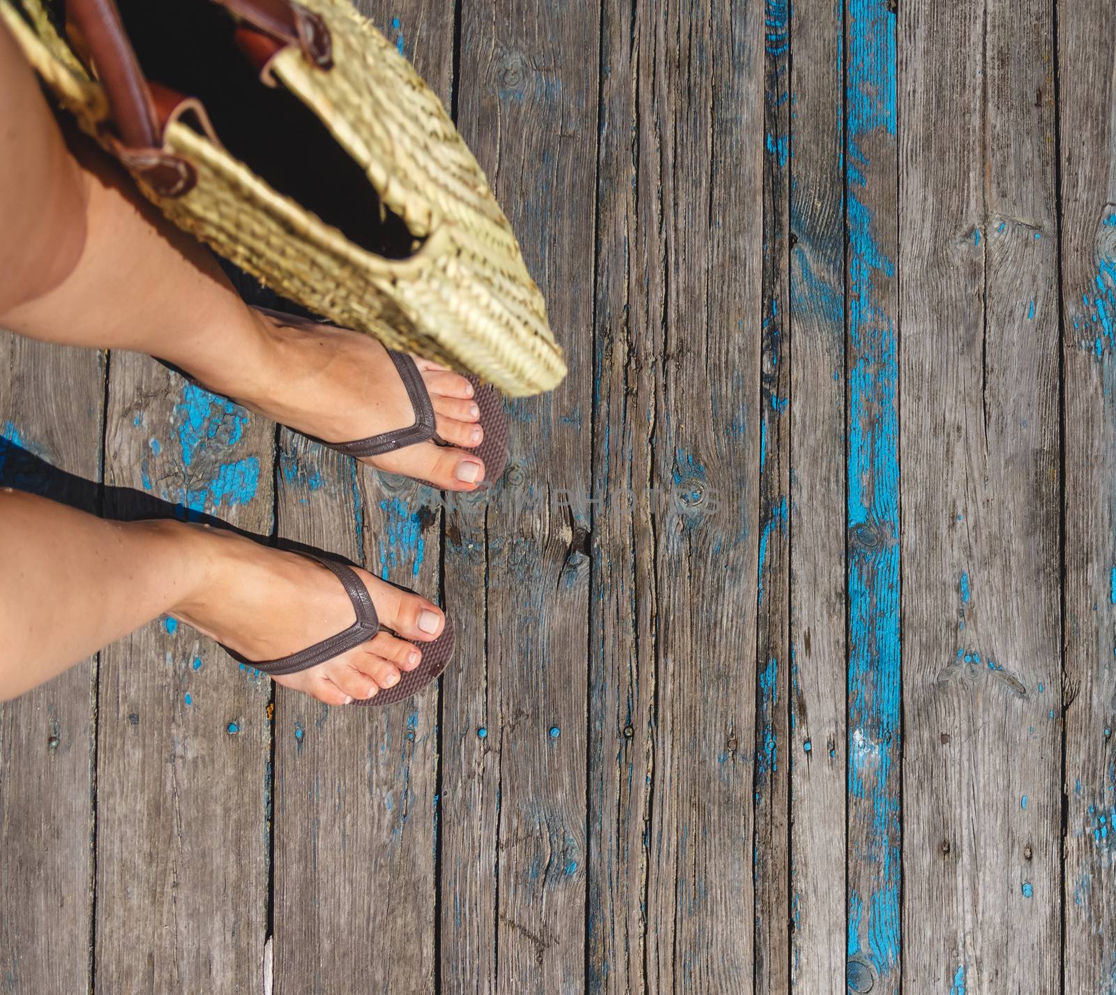 Top view, photo of legs in beach flip-flops and with a straw bag by Tanacha