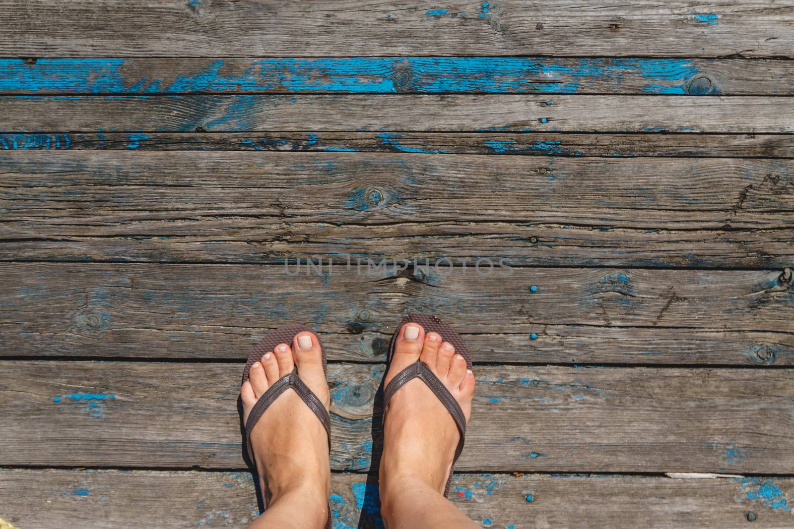 Top view, photo of female legs in beach flip flops on a wooden old floor. Photos on vacation, beach, summer.