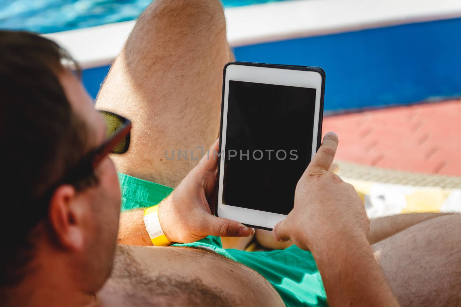 A young man in sunglasses holds a tablet in his hands. Freelancer job concept on the beach and vacation.