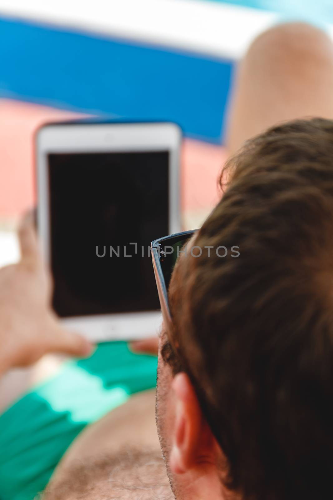 A young man in sunglasses holds a tablet in his hands. Freelancer job concept on the beach and vacation.