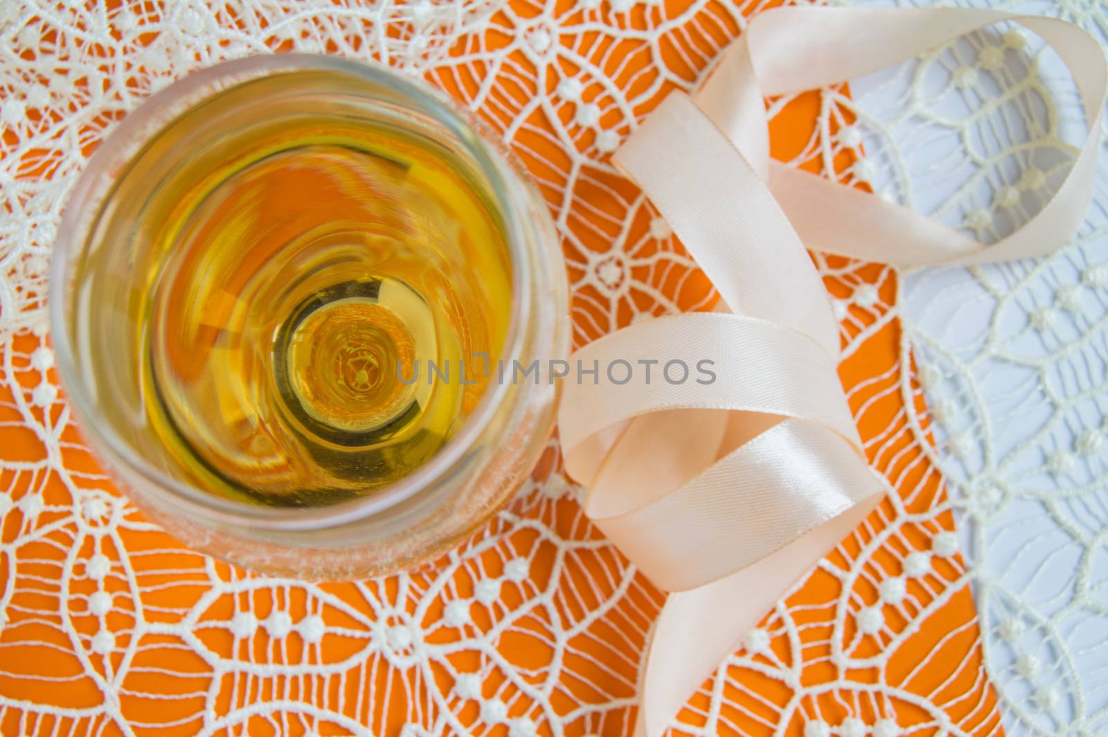 Flat stacking of white wine in a glass, beige lace and decorative ribbon, orange background, top view. Romantic spring or summer composition by claire_lucia