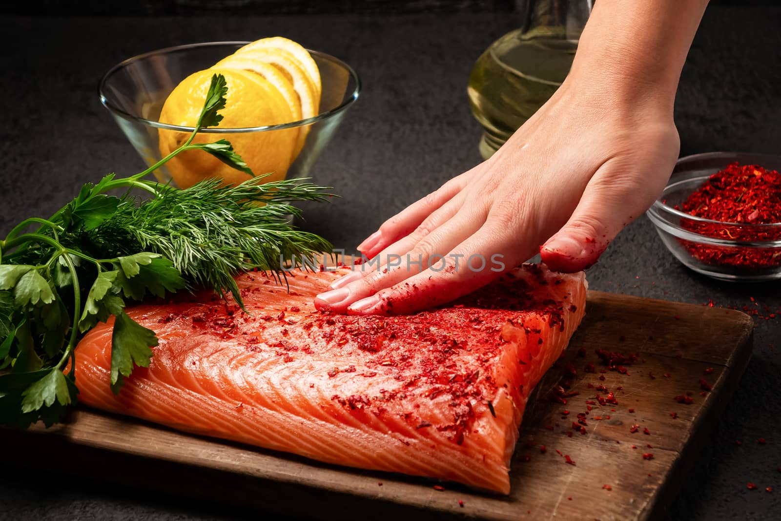 Female hand smears a piece of salmon fillet lying on a wooden cutting board with spices - photo, image by galsand