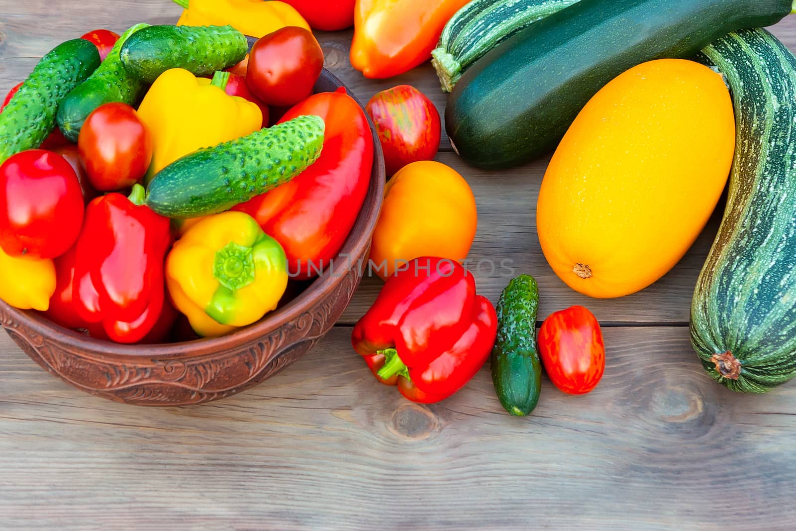 Vegetables: tomatoes, cucumbers, paprika, pepper, zucchini in a clay bowl and on a wooden table. Ingredients for the preparation of summer vegetable salad