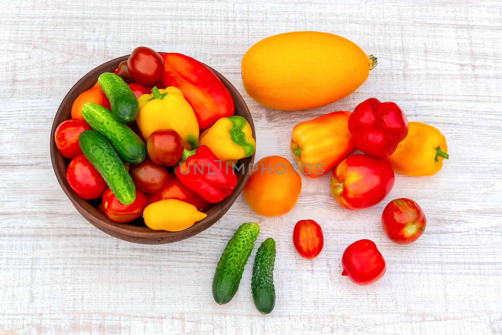 Vegetables: tomatoes, cucumbers, paprika, pepper, zucchini in a clay bowl and on a white wooden table. Ingredients for the preparation of summer vegetable salad