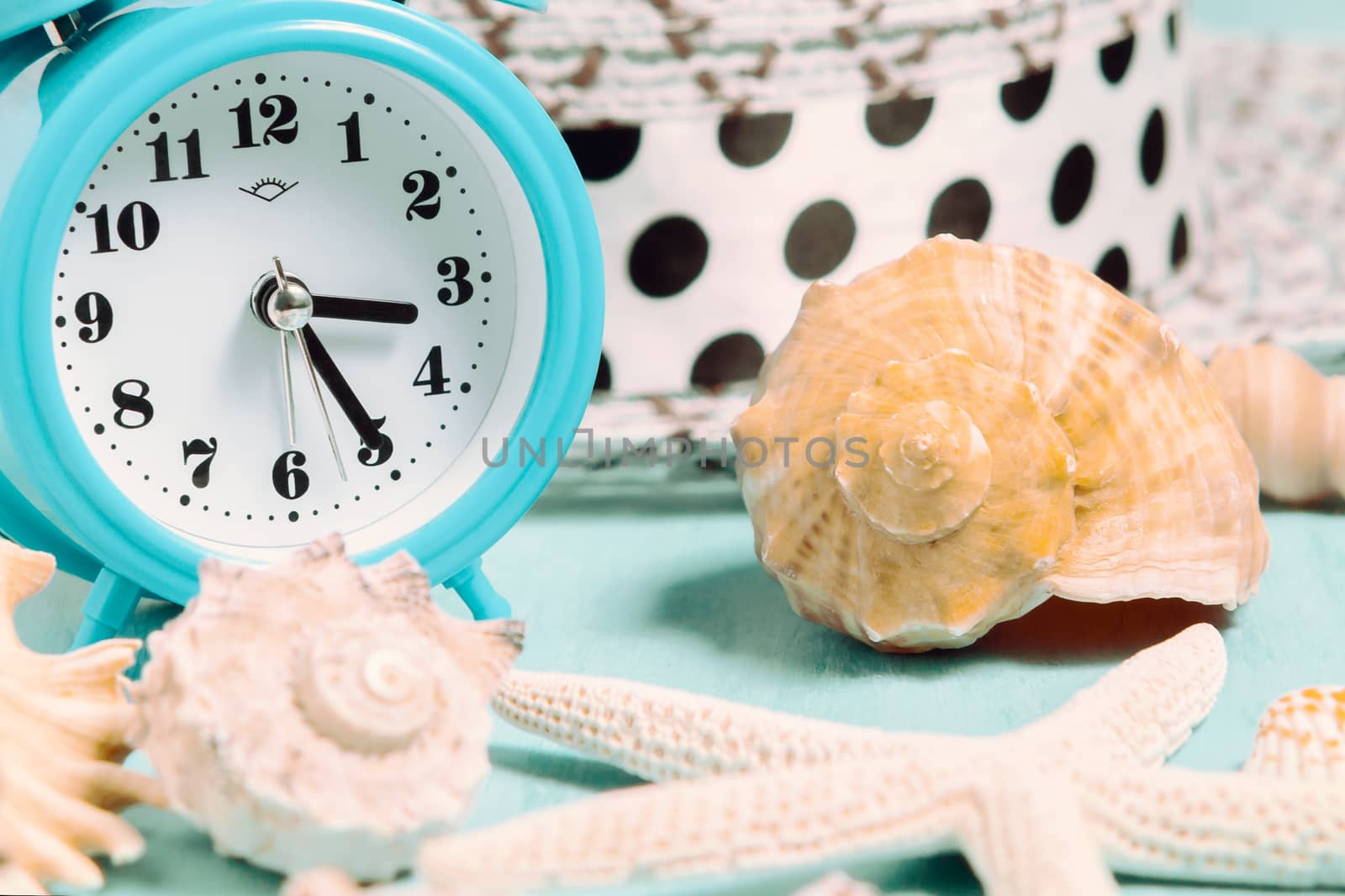 Seashells, alarm clock and beach accessories on a blue table - summer vacation and vacation time concept by galsand