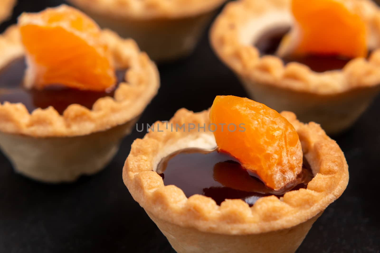 Sweet tartlets with chocolate and slices of tangerine on a dish of natural slate for serving, close-up.