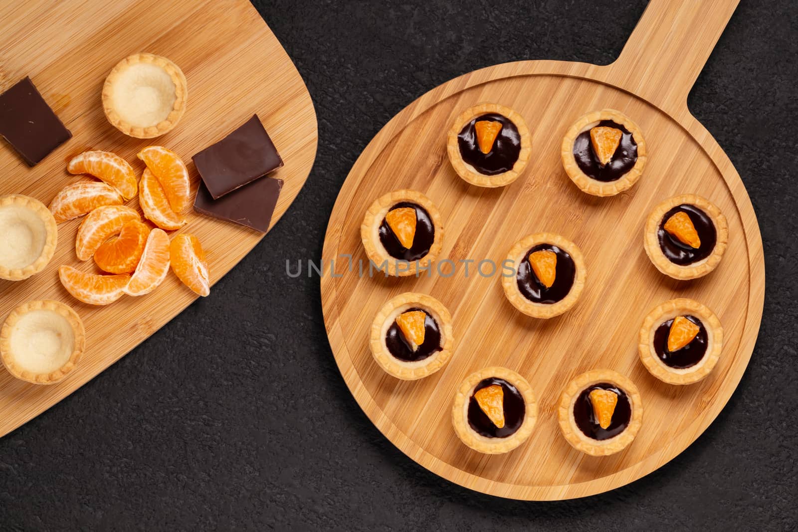 Sweet tartlets with chocolate and slices of tangerine on a wooden dish for serving, top view by galsand