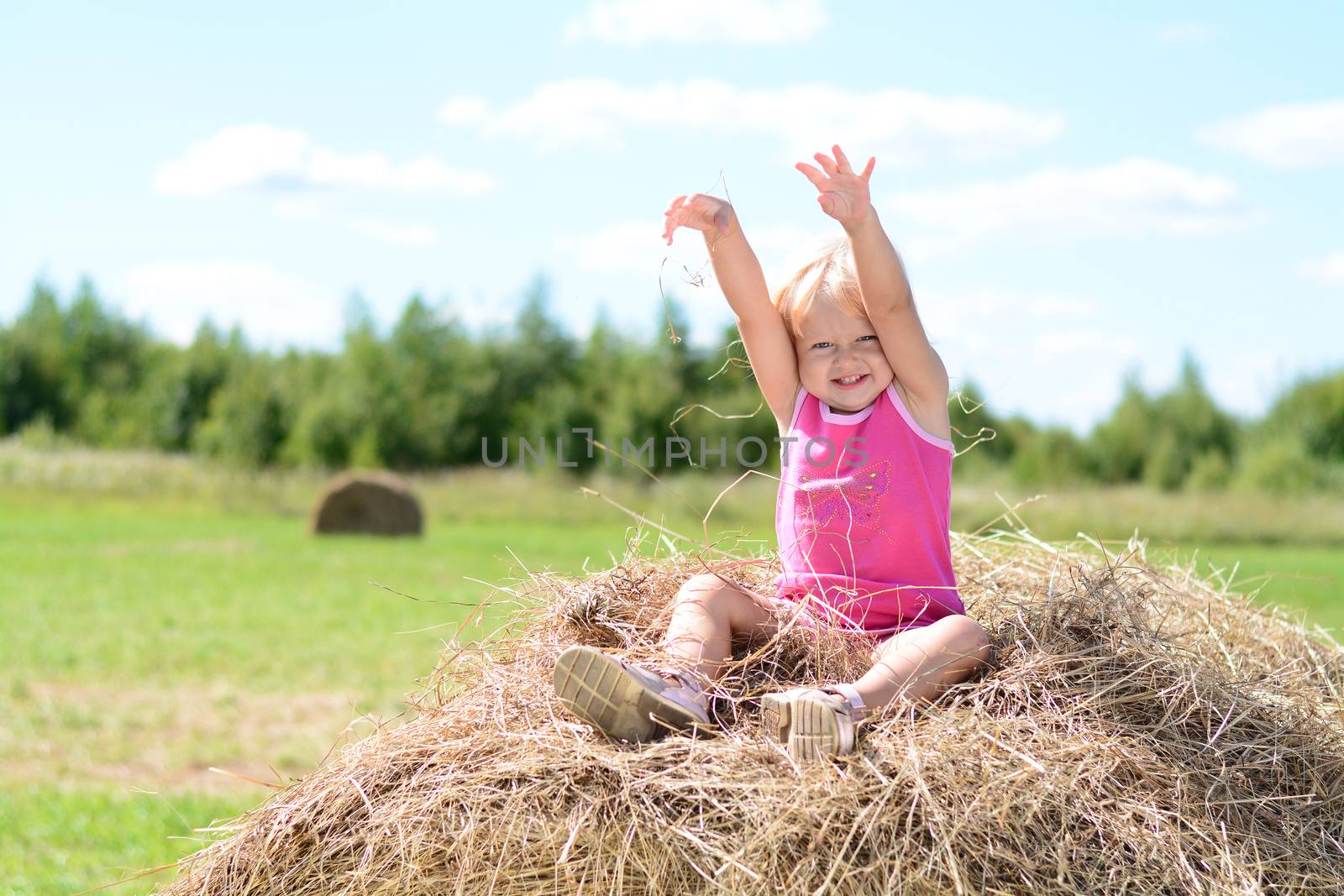 Happy baby girl laughing on hay in summer haystack